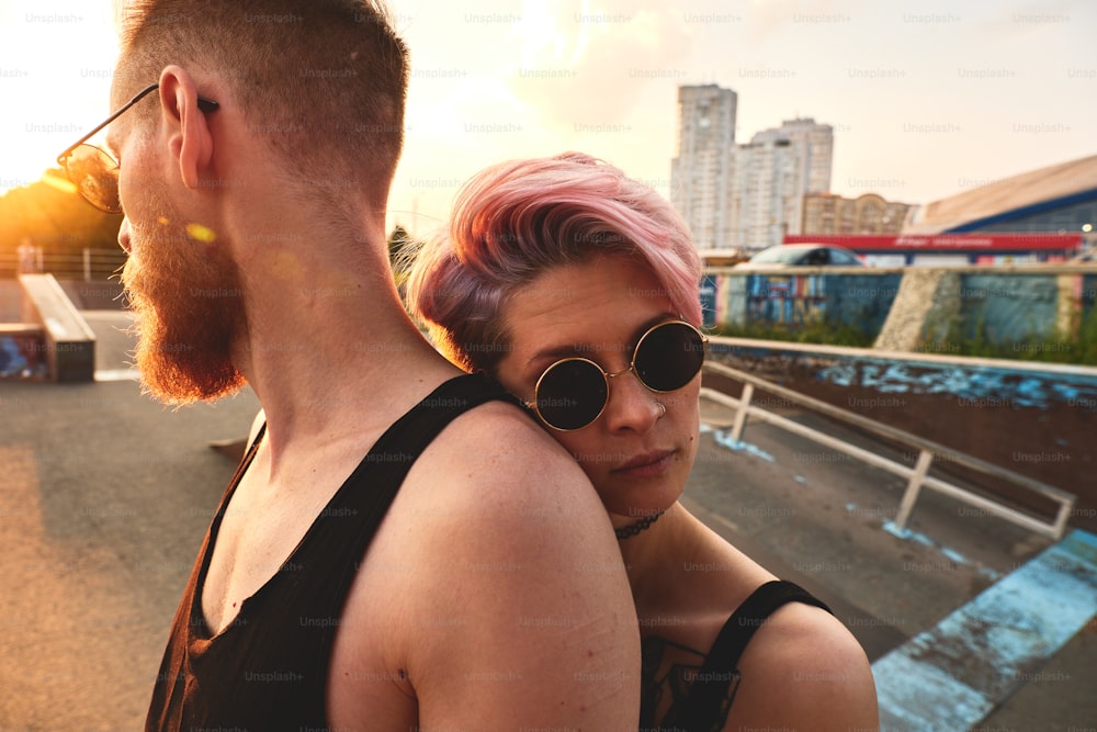 Portrait of pink haired girl and auburn man together outdoor. She is leaning on his back, trust and confidence concept