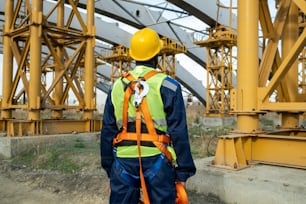 Rear view of construction worker in equipment and in work helmet working on construction site