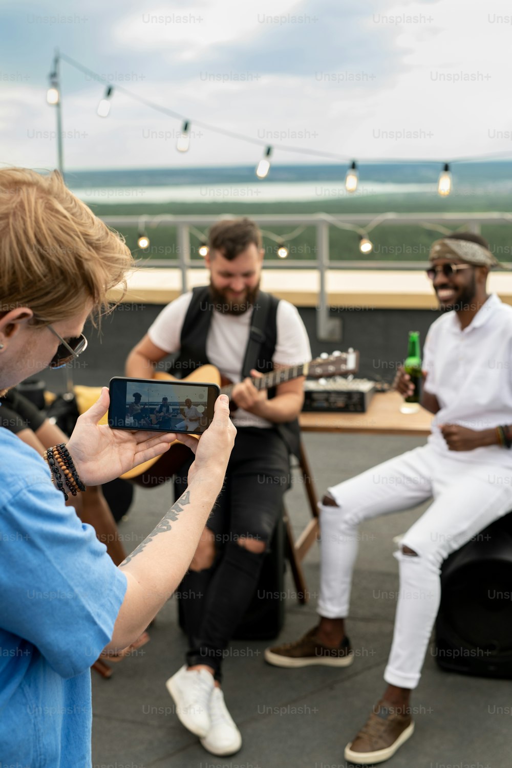 Young man shooting video on smartphone of his happy friends enjoying rooftop party