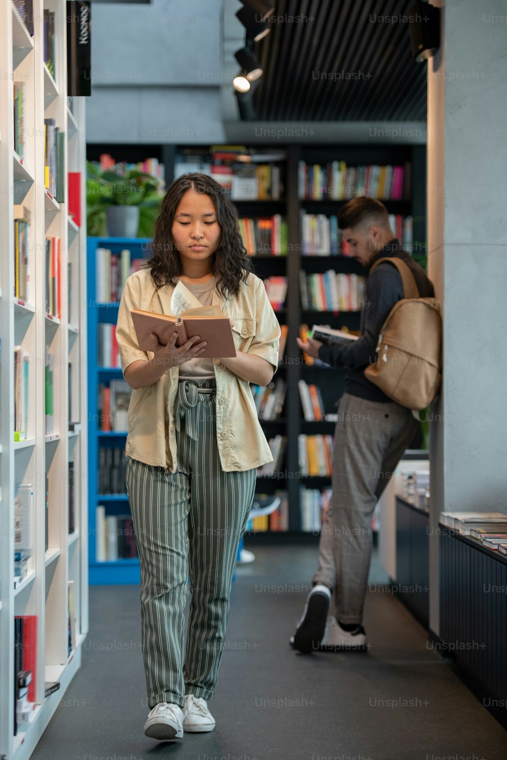 Young female reading book on the move against male student in library