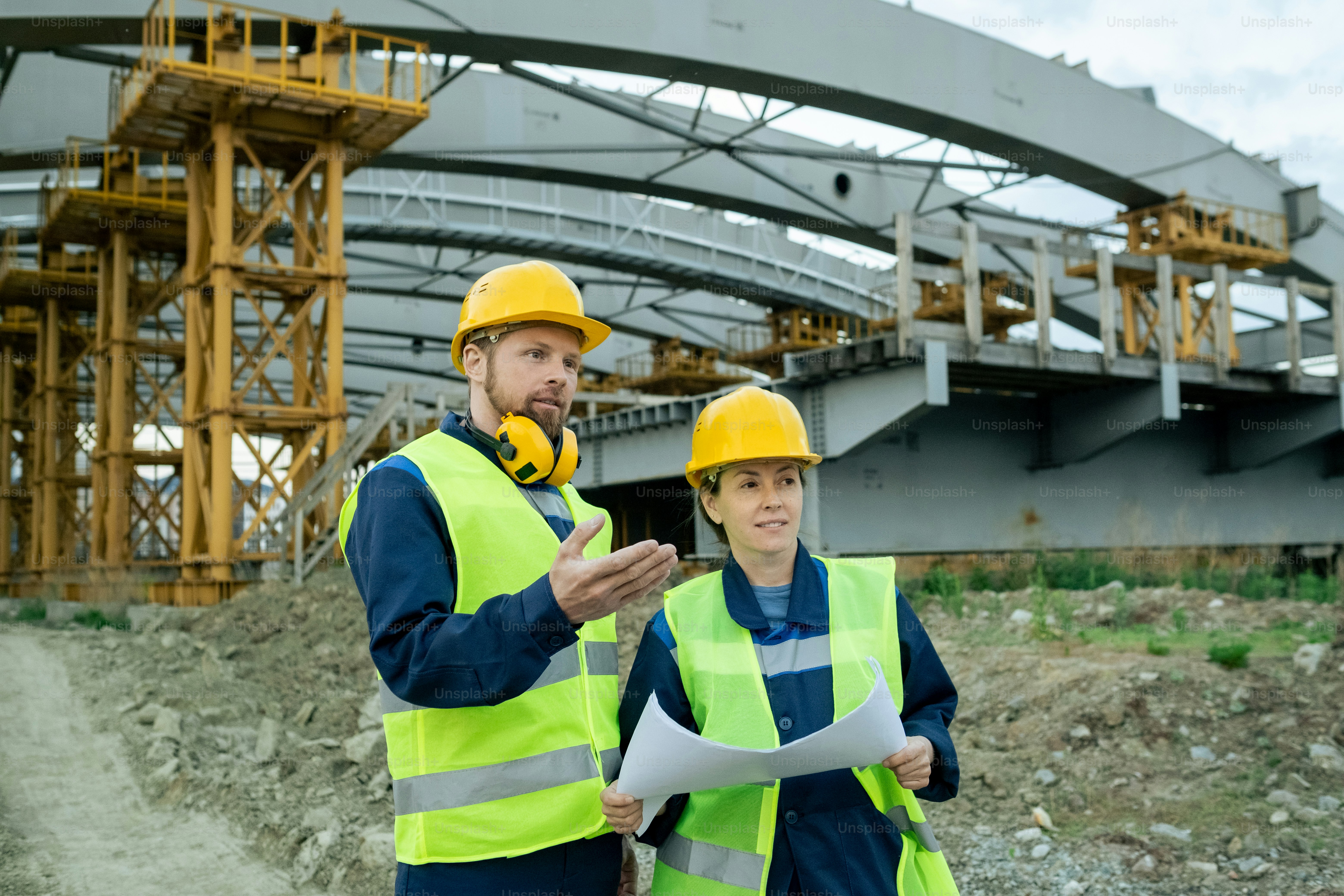 Bauarbeiter in reflektierender Kleidung und Arbeitshelmen betrachten das Gebäude und prüfen den Bauplan auf der Baustelle