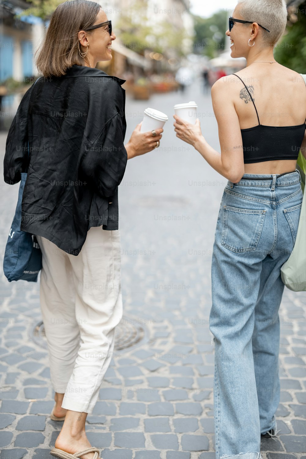 Stylish lesbian couple walking the street and holding hands together. View from the backside. Street fashion and lifestyle, homosexual relations