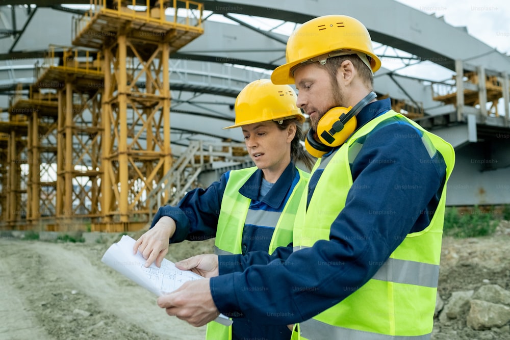 Two workers in work helmets examining blueprint during their work on construction site