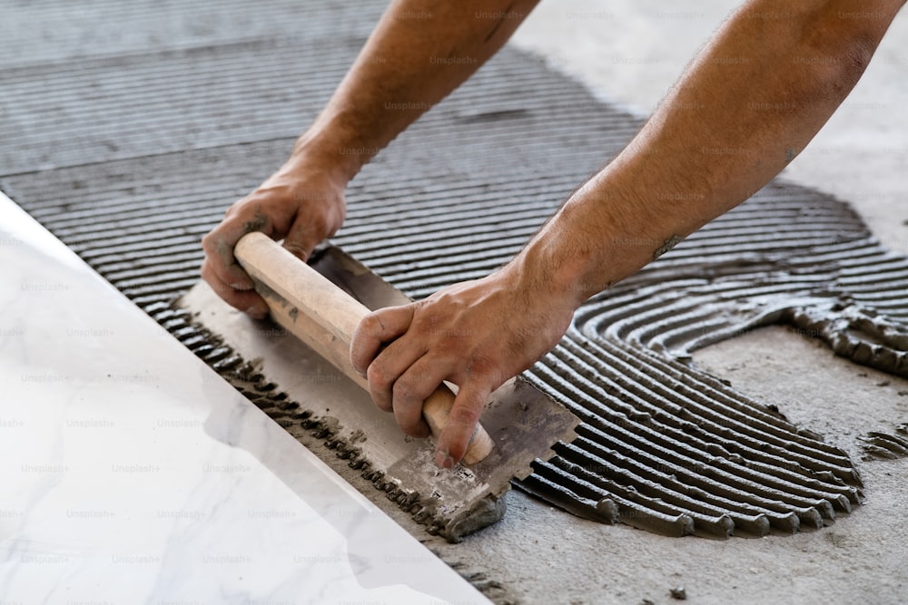 Laying Ceramic Tiles. Troweling mortar onto a concrete floor in preparation for laying white floor tile.