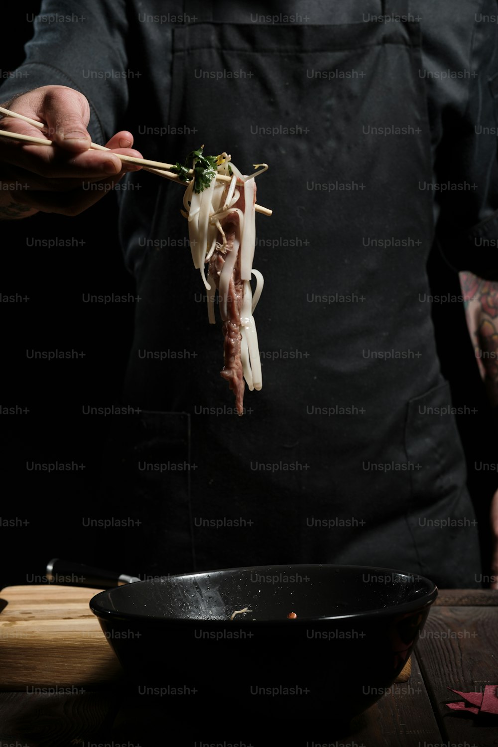 Primer plano de las manos del chef degustando el tazón de fideos de ternera con palillos