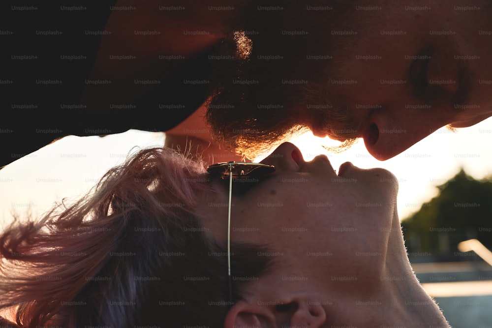 Nahaufnahme Porträt eines jungen Paares, eines rothaarigen Jungen und eines rosahaarigen Mädchens, die dicht beieinander auf dem Boden liegen und sich um einen Kuss bemühen