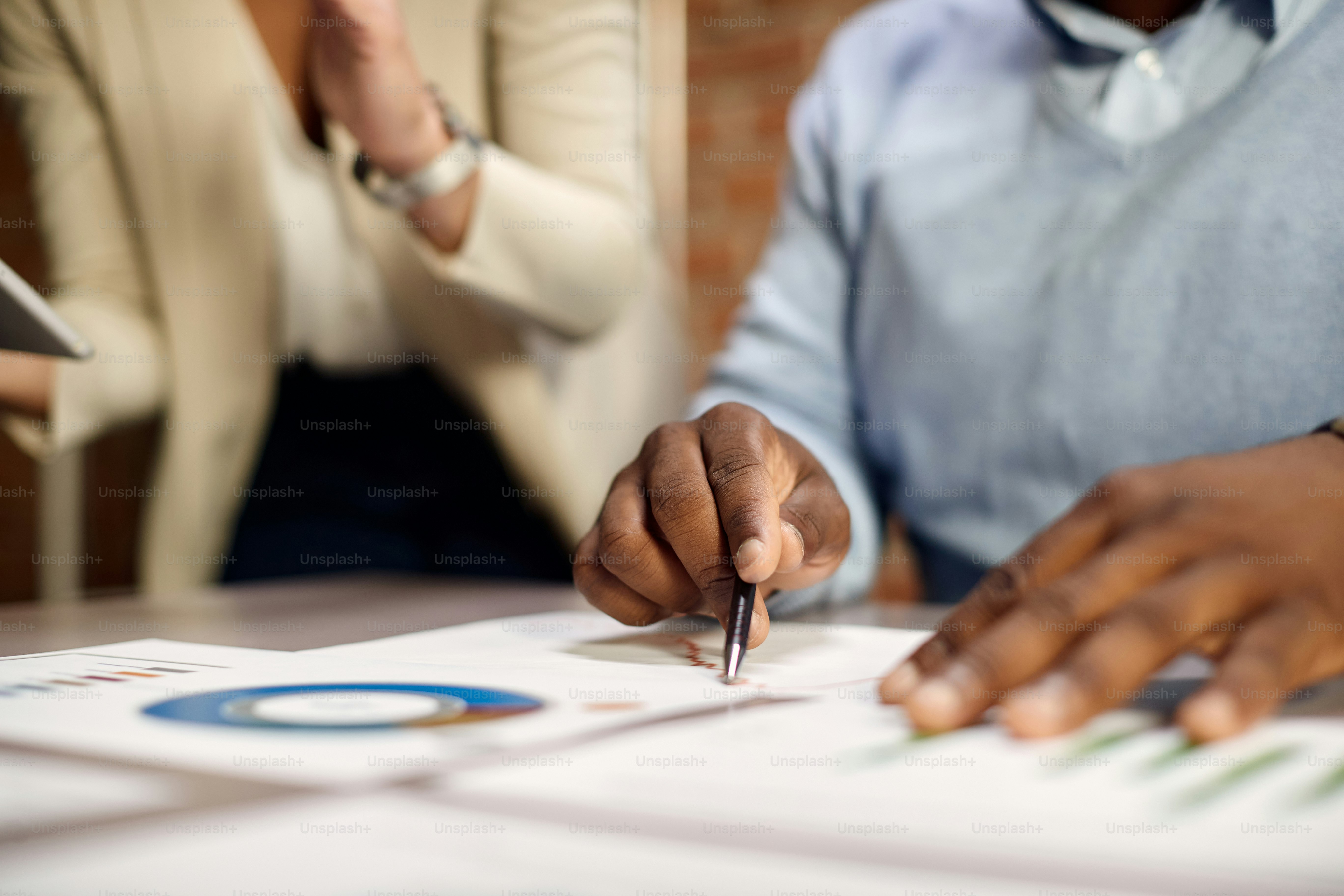 Nahaufnahme eines afroamerikanischen Geschäftsmannes mit einem Kollegen, der Berichte im Büro analysiert.