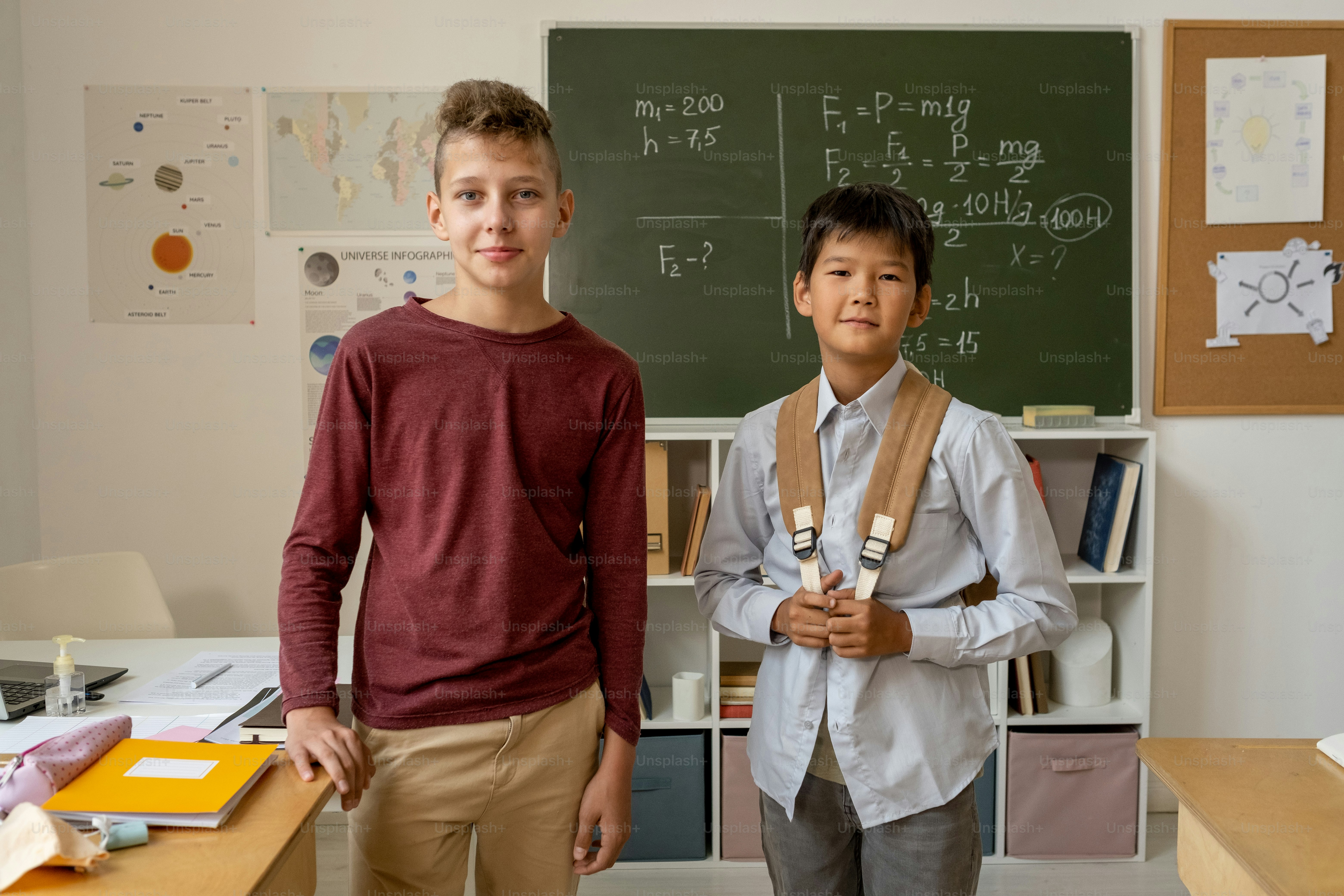 Two handsome schoolboys in casualwear looking at you in classroom