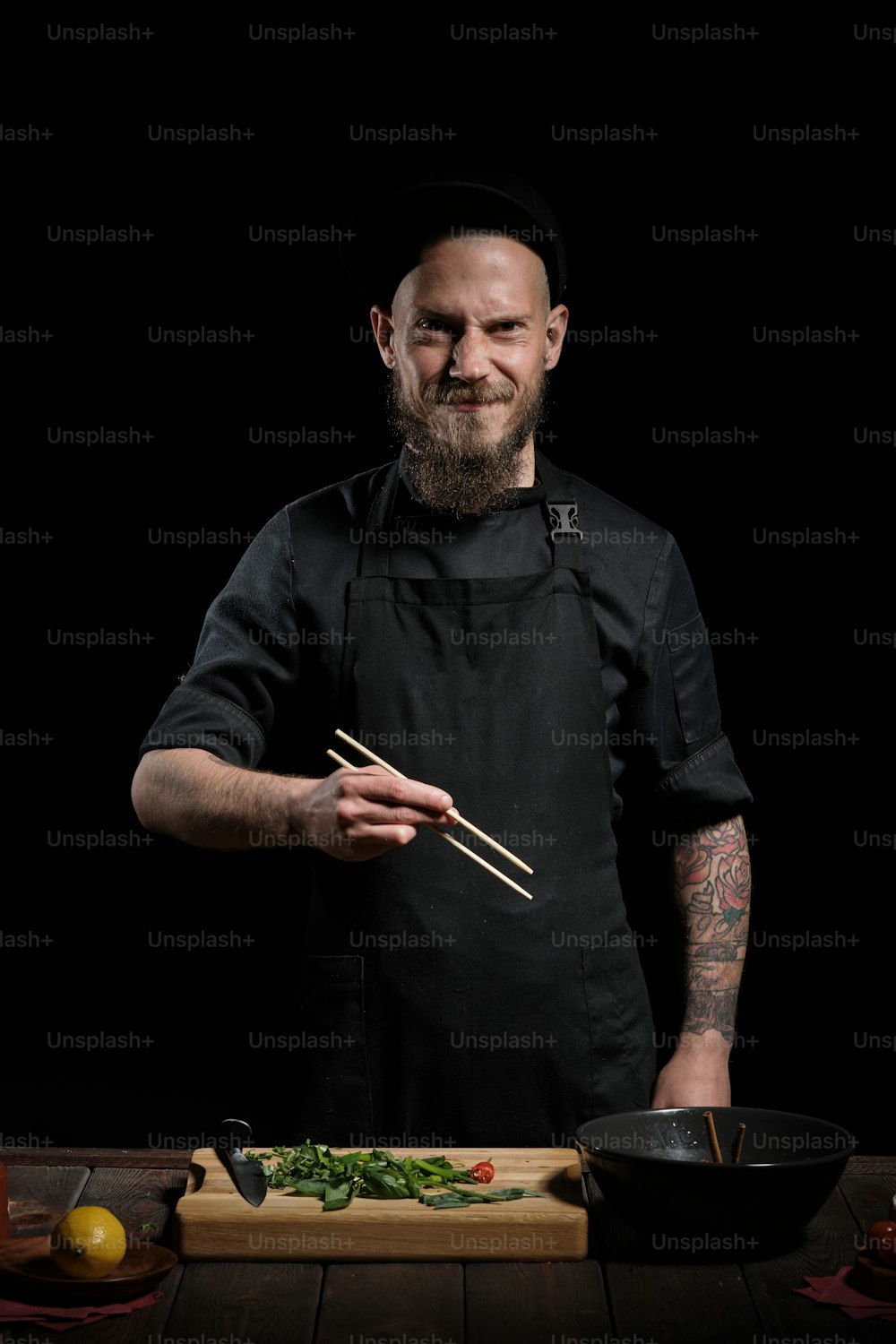 Ritratto di chef maschio che cucina pho bo in studio, tenendo le bacchette, su sfondo nero