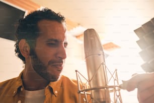 Portrait of moroccan man in yellow shirt singing with microphone in professional recording studio