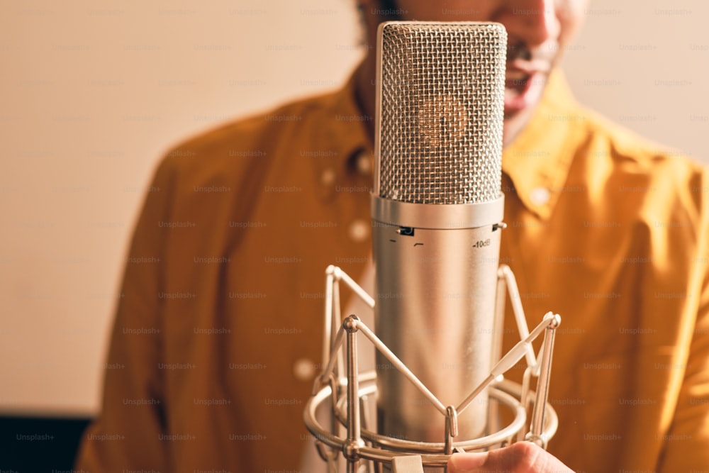 Close up do homem marroquino na camisa amarela cantando com microfone no estúdio de gravação profissional