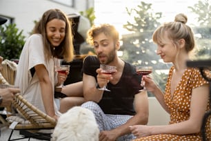 Young friends hanging out together, sitting with a dog, drinking wine and talking. People spending summer time having lunch together at backyard of country house at sunset
