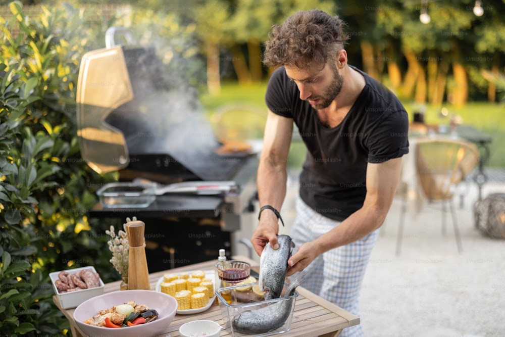 Men preparing fish for a grill, cooking healthy sea food and vegetables on a modern gas grill at backyard on nature