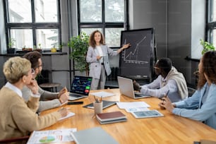 Young successful business coach with tablet showing graph on blackboard