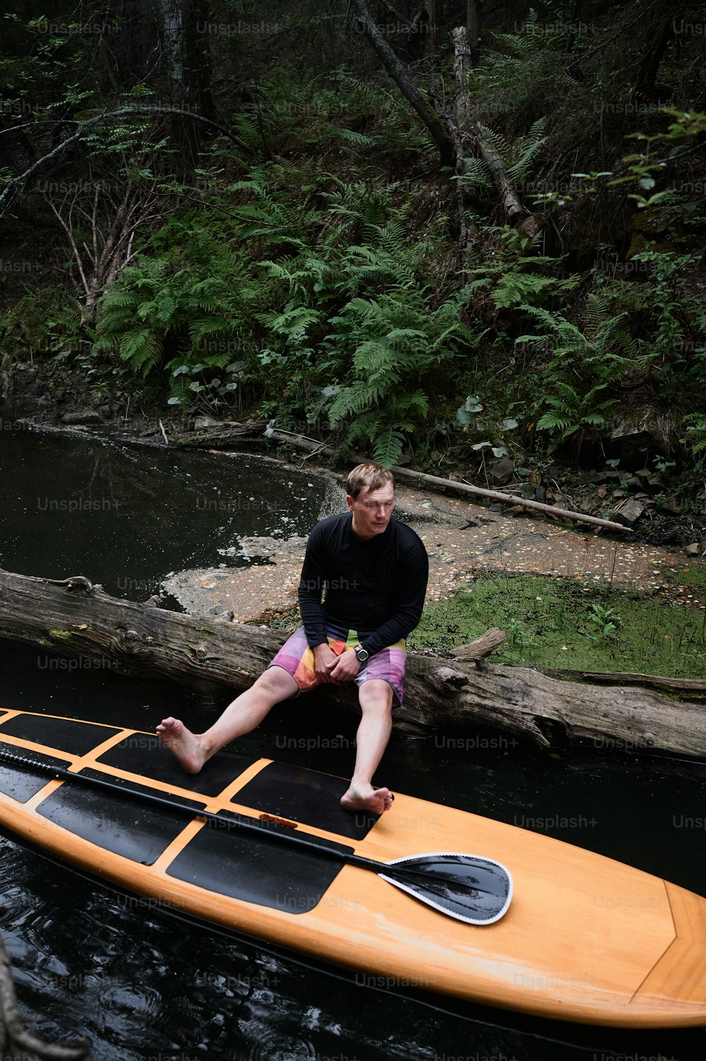 上の写真は、ボードの上でパドリングしながら休憩している男性の写真です。彼は荒れ狂う川岸に座っていて、足はサップボードの上に乗せられています