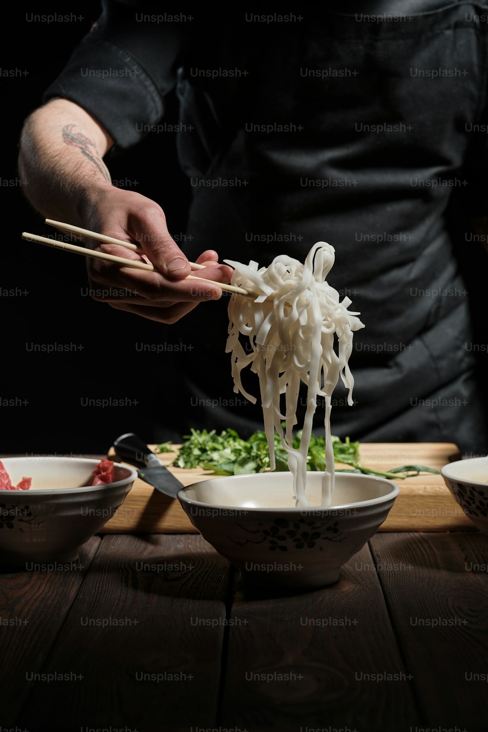 Primo piano delle mani dello chef che raccolgono le tagliatelle dalla ciotola, preparando il cibo asiatico