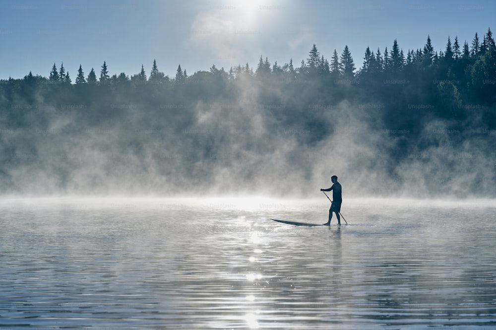 早朝、山に霧が立ち込めるサーフボードを漕ぐ男性のシルエット