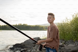 Adolescente contemporáneo con caña larga pescando solo por el lago en el fin de semana de verano