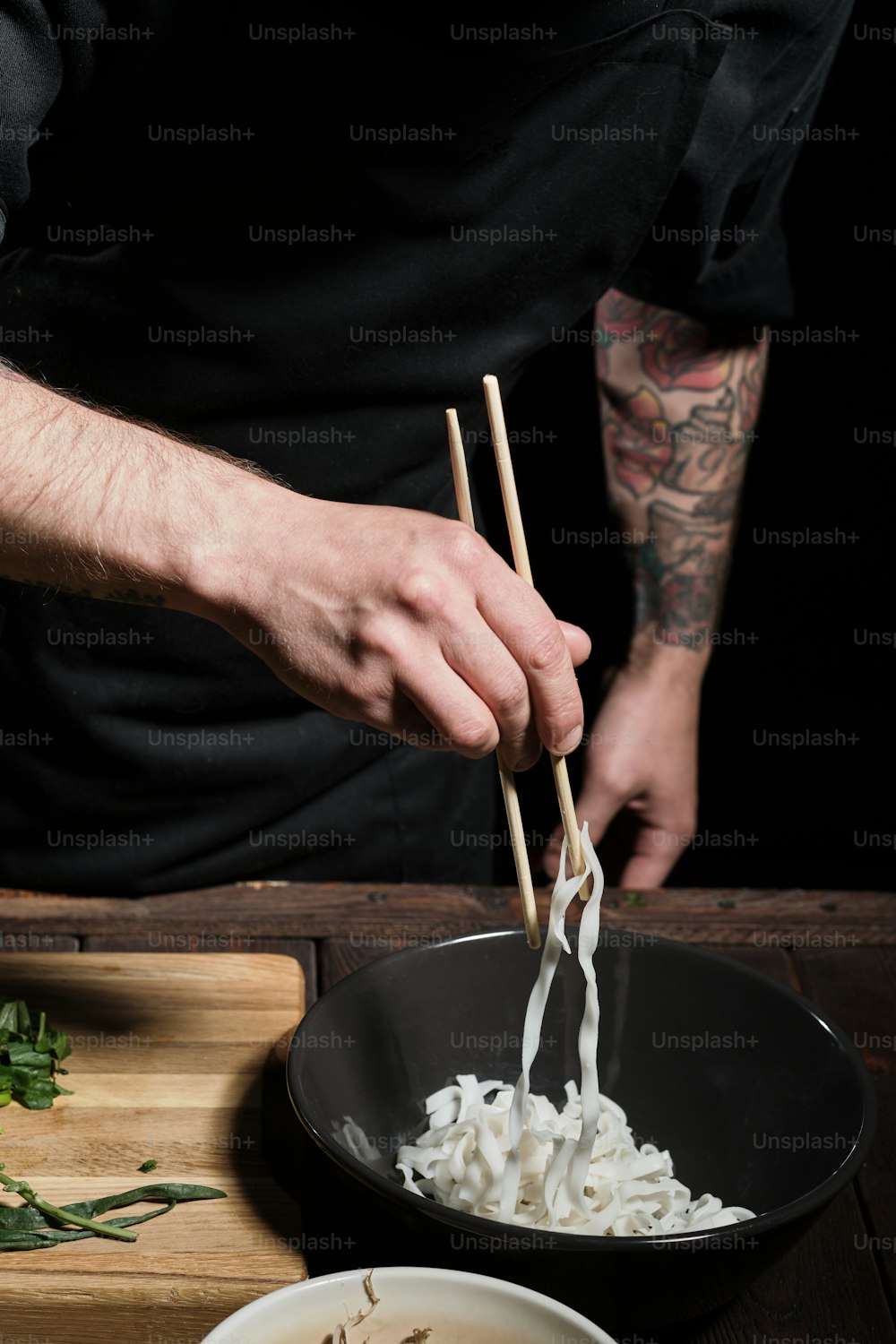 Primer plano de las manos del chef recogiendo fideos del tazón, preparando comida asiática