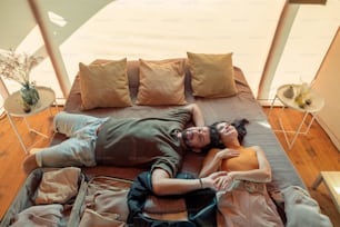 Glückliches Paar beim Tagträumen im Bett mit ausgepacktem Gepäck