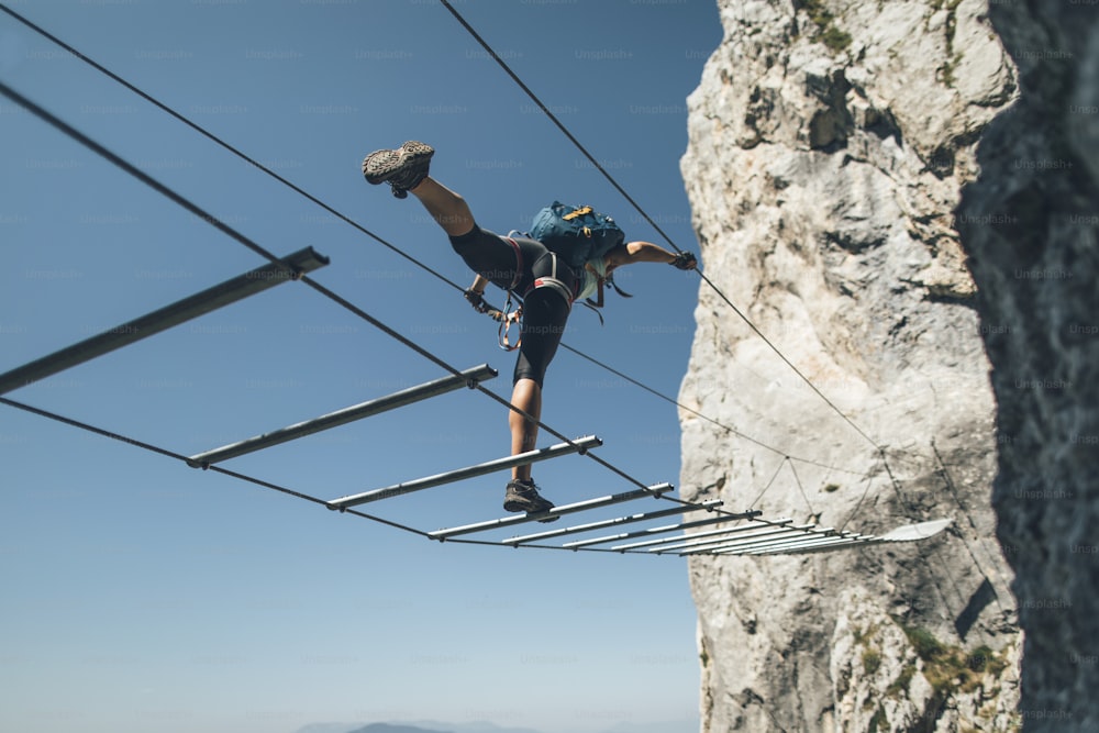 Woman climber posing on via ferrata  suspended wire bridge.