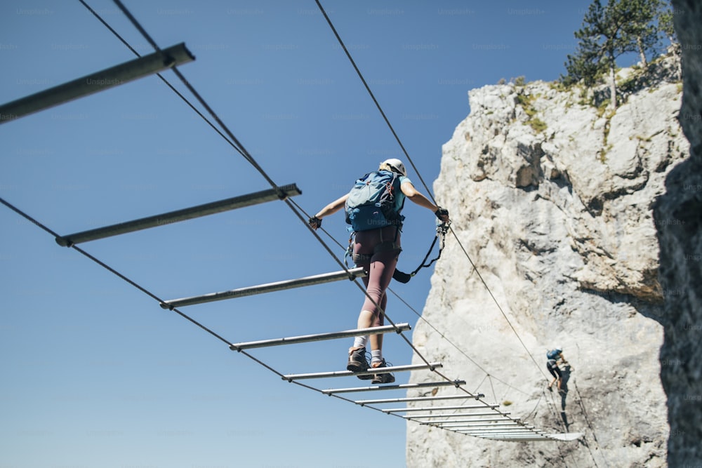 Climber on via ferrata  crossing suspended wire bridge.