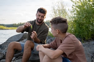 Père heureux avec un appât de pêche regardant son fils adolescent tout en expliquant comment l’utiliser