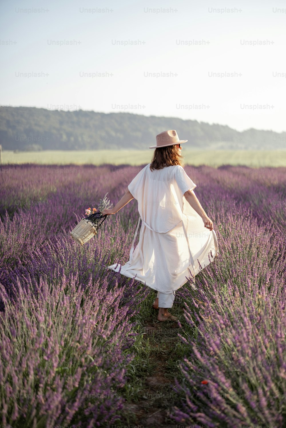 Mujer joven que camina en el campo de lavanda con ramo de flores violetas y disfruta de la belleza de la naturaleza. Calma y concepto consciente. Espacio de copia