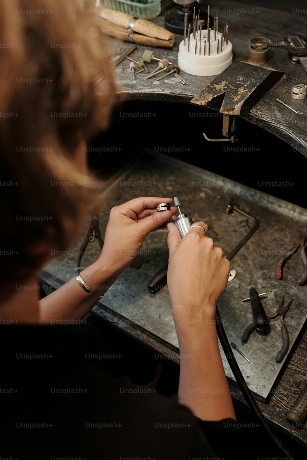 Vue par-dessus l’épaule d’un bijoutier de fabrication méconnaissable polissant une bague en argent dans un atelier