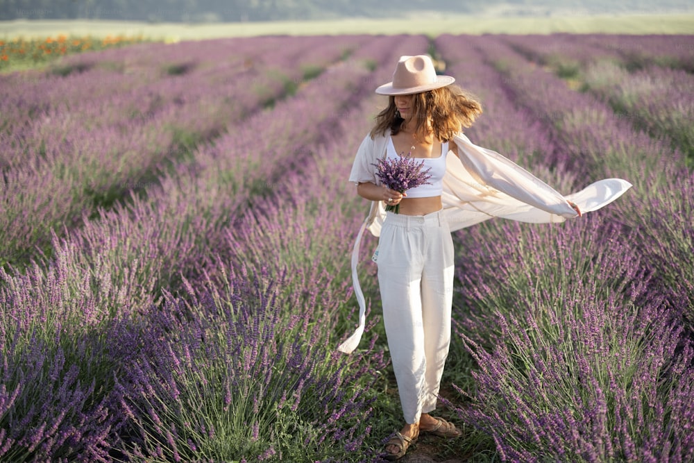 Mujer joven bailando en el prado de lavanda con ramo de flores violetas y disfruta de la belleza de la naturaleza. Calma y concepto consciente