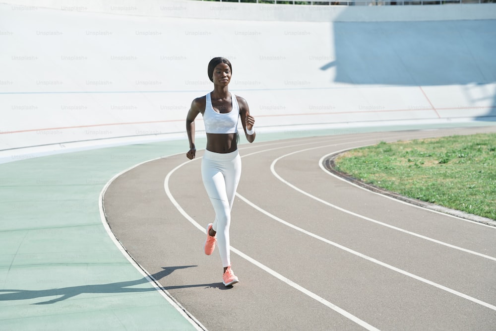 Giovane donna africana fiduciosa in abbigliamento sportivo che corre in pista all'aperto