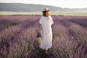 Young woman staying back on lavender field with bouquet of flowers and enjoy the beauty of nature. Calmness and mindful concept.