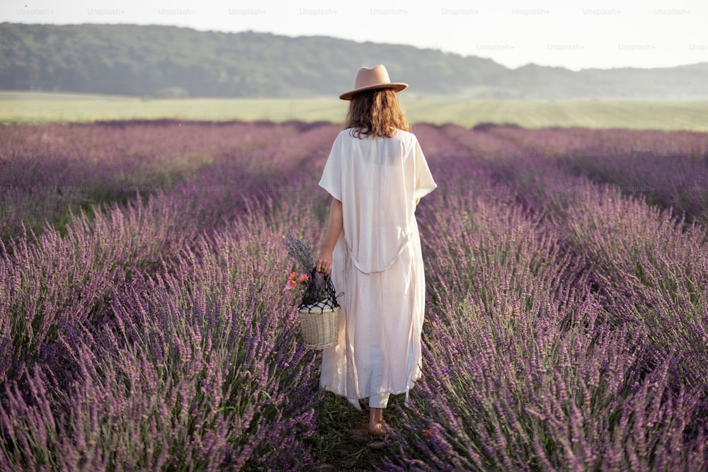 Mujer joven que se queda atrás en el campo de lavanda con ramo de flores y disfruta de la belleza de la naturaleza. Calma y concepto consciente.