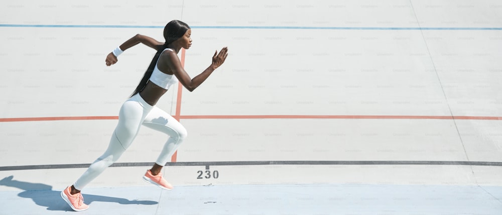 Confident young African woman in sports clothing running on track outdoors