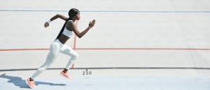 Confident young African woman in sports clothing running on track outdoors