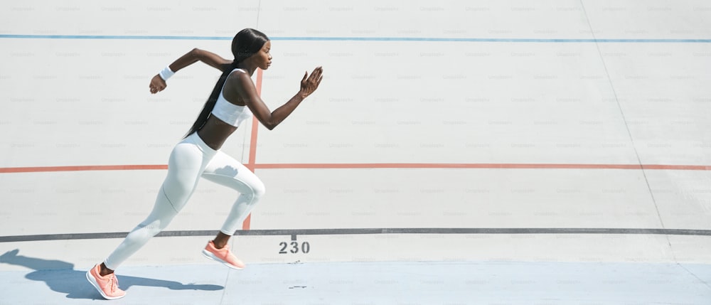 Giovane donna africana fiduciosa in abbigliamento sportivo che corre in pista all'aperto