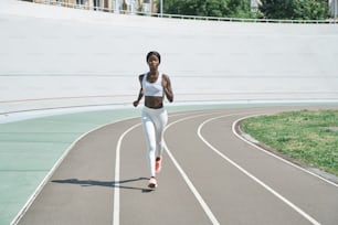 Full length of beautiful young African woman in sports clothing running on track outdoors