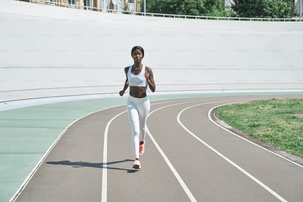 Full length of beautiful young African woman in sports clothing running on track outdoors