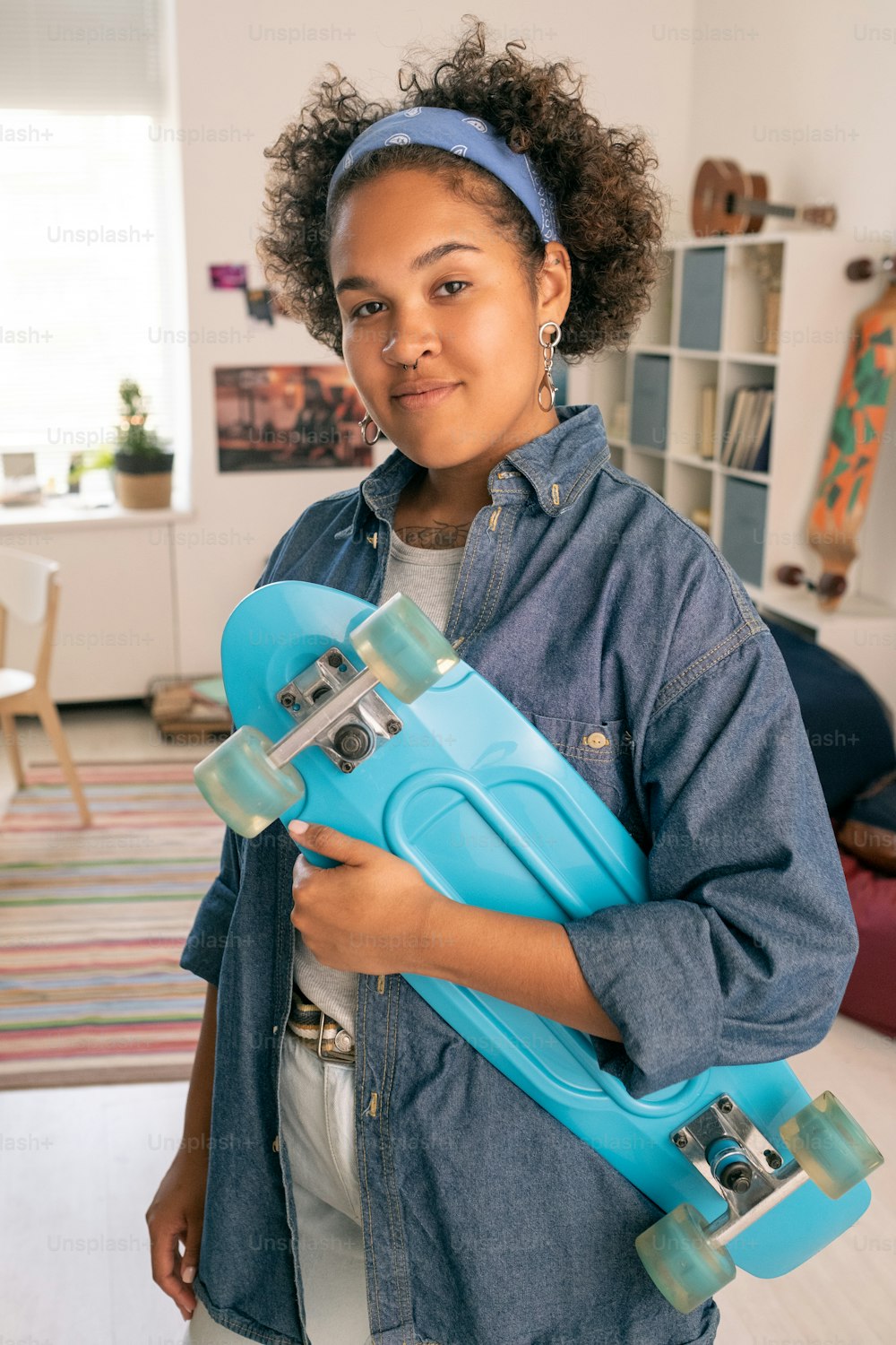 Happy African teenage girl in casualwear holding blue skateboard