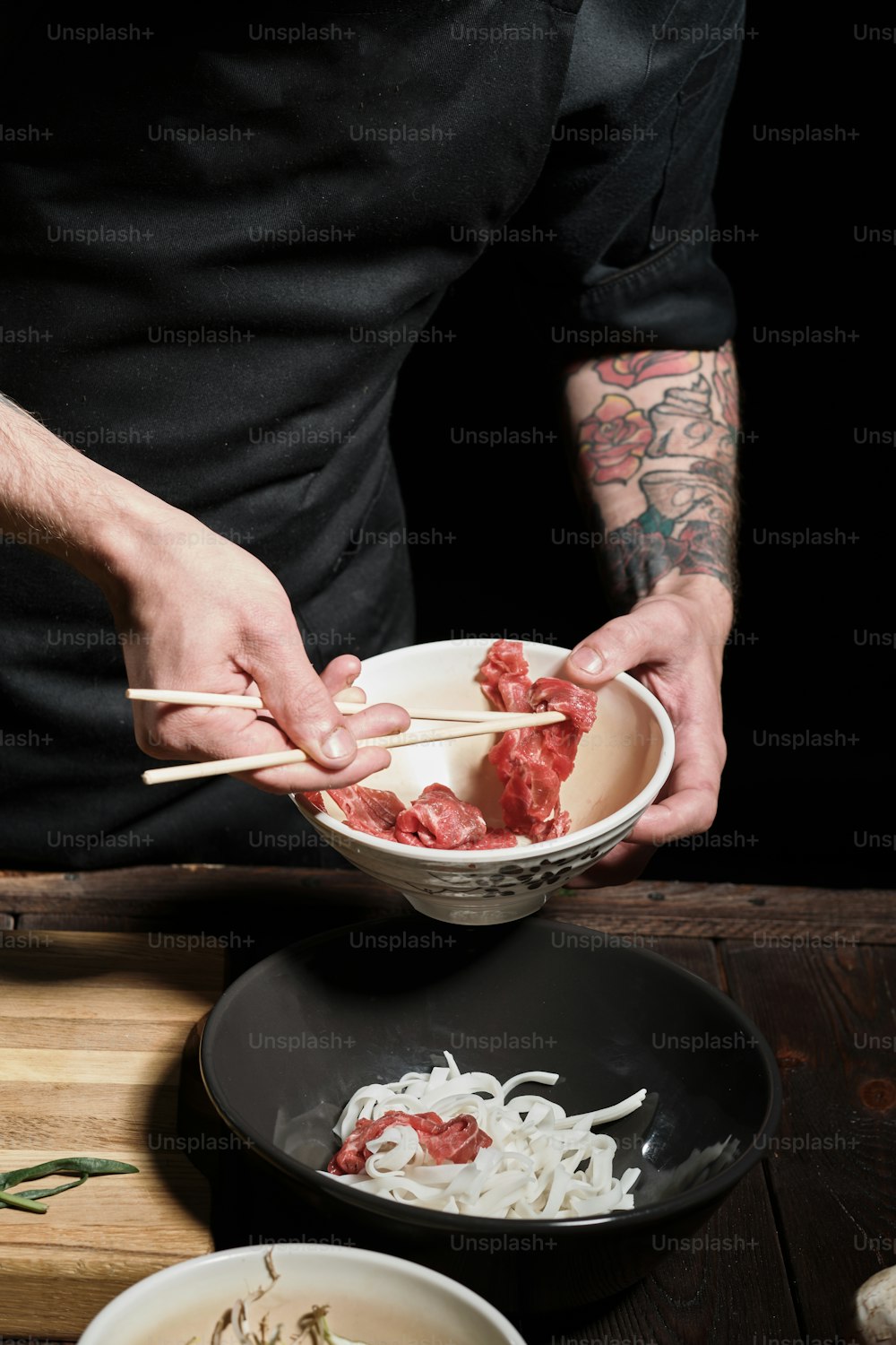 Close up of chef's hands adding beef to noodle bolw with chopsticks