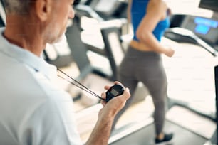 Close-up of fitness instructor using stopwatch while woman is running on treadmill in a gym.