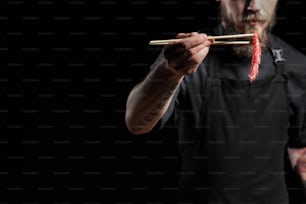 Primer plano del chef sosteniendo un trozo de ternera con palillos, cocinando un plato asiático fresco