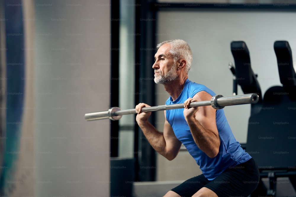Mature athlete exercising with barbell during strength training in gym.