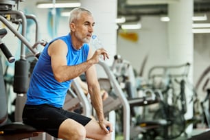 Mature athletic man drinking water on a break during sports training in a gym.