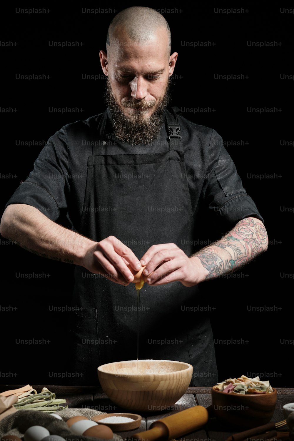 Portrait of chef in studio on black. He is making fresh dough