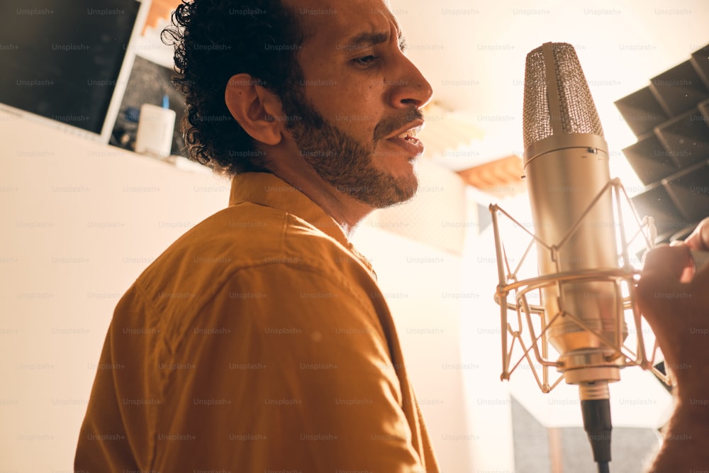Porträt eines marokkanischen Mannes im gelben Hemd, der mit Mikrofon im professionellen Aufnahmestudio singt