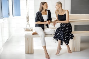 Lesbian couple sitting and talking together, holding hands, having leisure time at modern studio apartment. Homosexual relations and comfort living at home