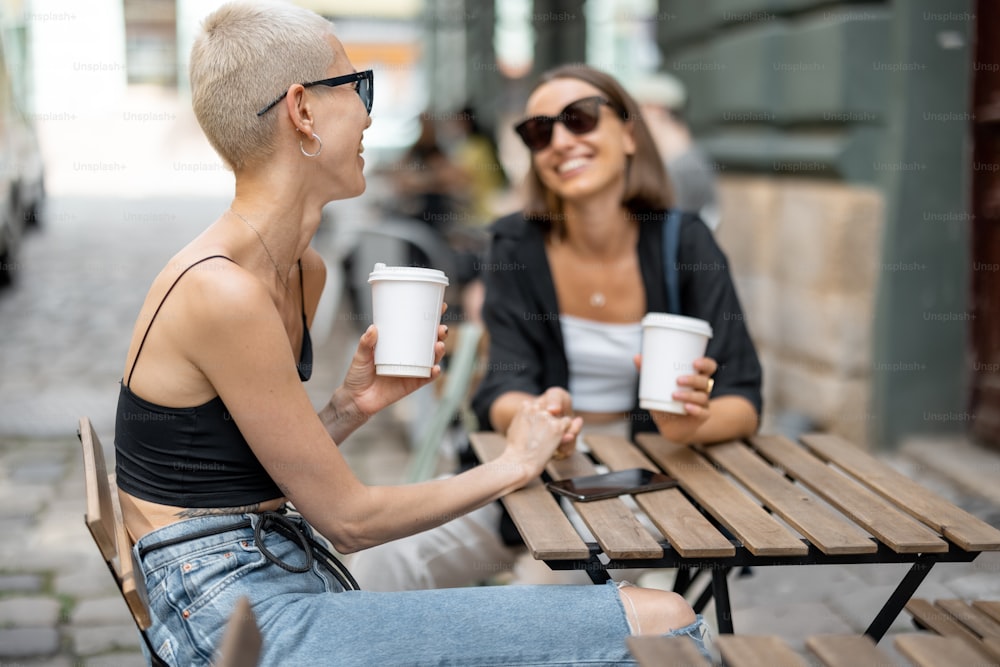 Stylish female couple having fun, drinking coffee at cafe outdoors. Homosexual relation and leisure time in the city