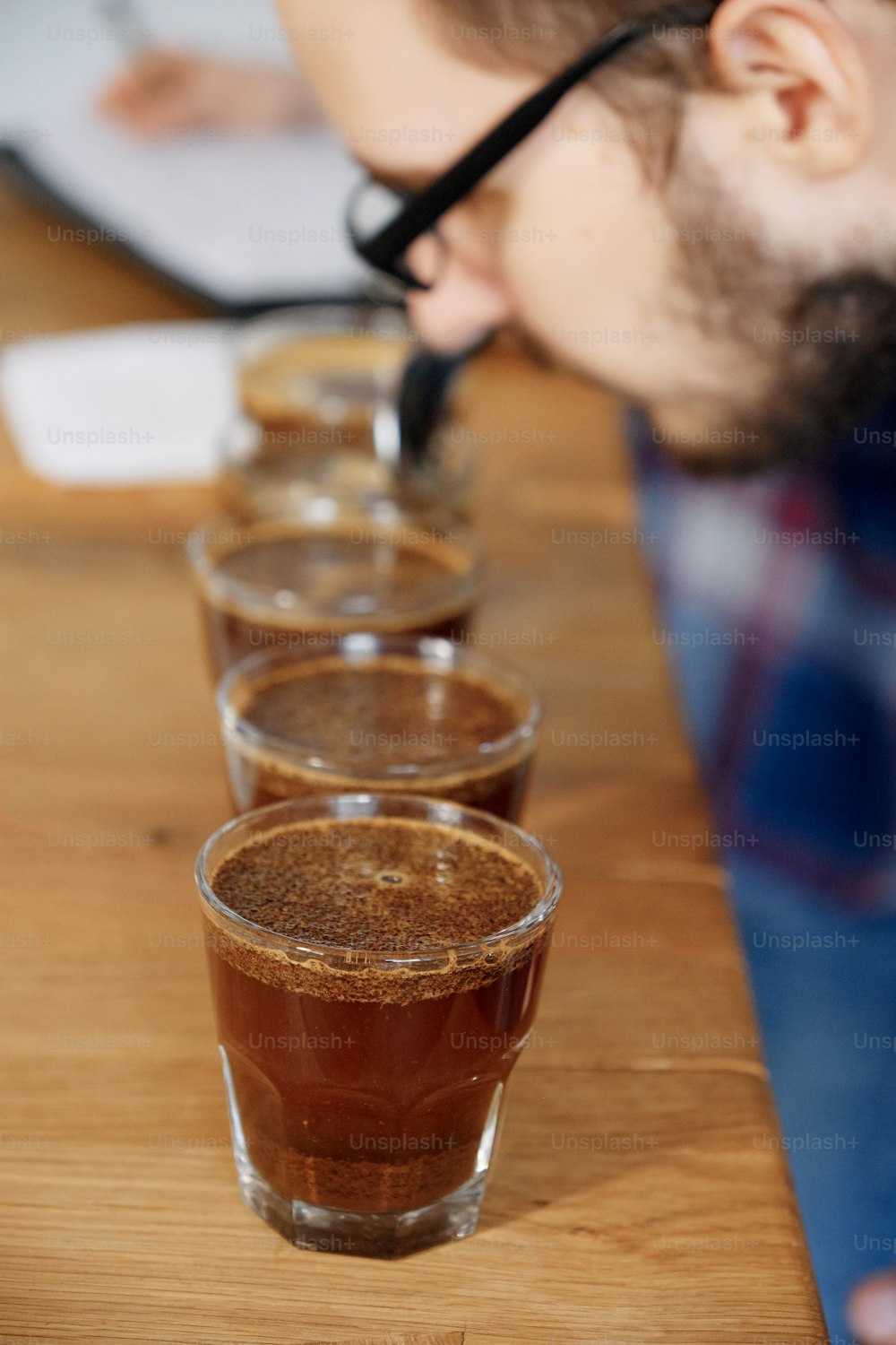 Portrait of man smelling freshly brewed coffee in glass cup, using spoon, examining coffee taste and flavour at coffee cupping test for barosta