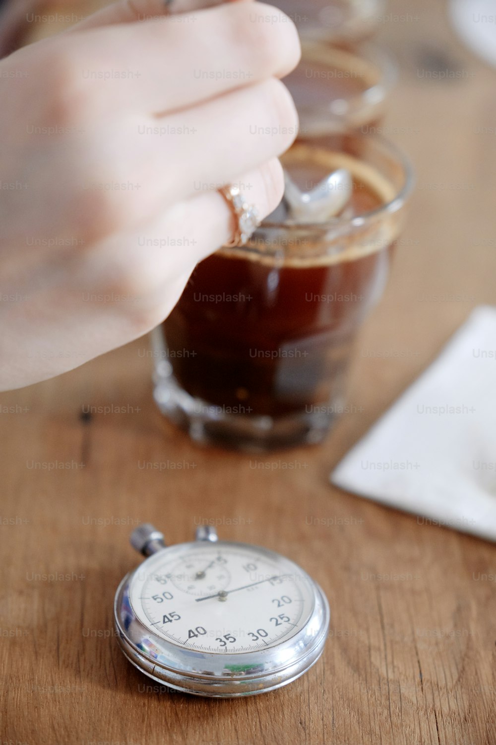 ガラスのコップで淹れたてのコーヒーを味わう男の手の接写、スプーンの使用、バロスタのコーヒーカッピングテストでのコーヒーの味と風味の検査